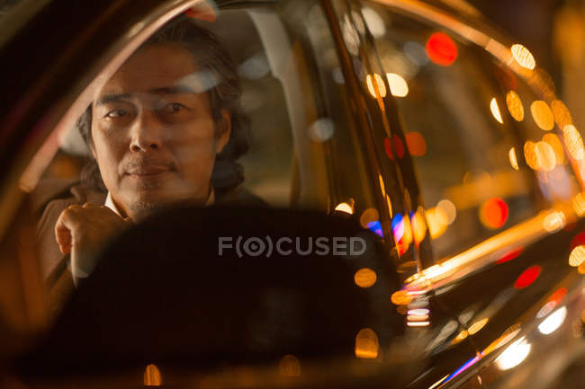 Sérieux mature asiatique l'homme assis dans voiture la nuit, sélectif focus — Photo de stock