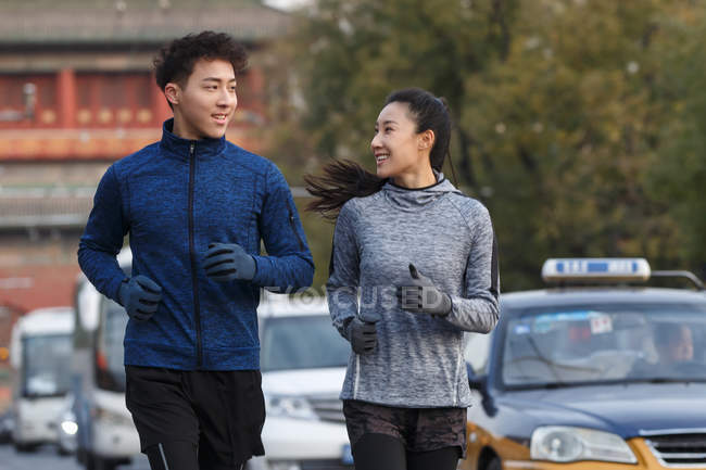 Feliz deportivo joven asiático pareja sonriendo uno al otro y corriendo juntos en la calle - foto de stock