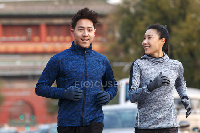 Vista frontal de sonriente joven pareja asiática en ropa deportiva corriendo juntos en la calle - foto de stock