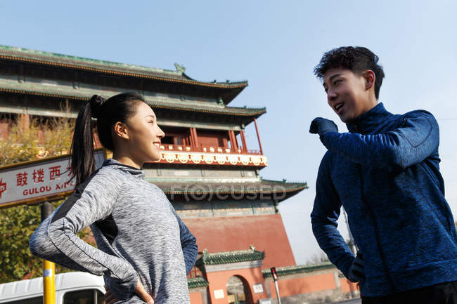 Low angle view of spoty young asian couple talking and smiling each other during workout on street — Stock Photo