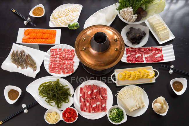 Vista de ángulo alto de varios ingredientes, carne, verduras, mariscos y olla caliente de cobre, concepto de plato de roce - foto de stock