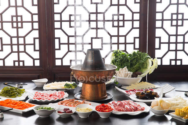 Plates with various ingredients and copper hot pot, chafing dish concept — Stock Photo