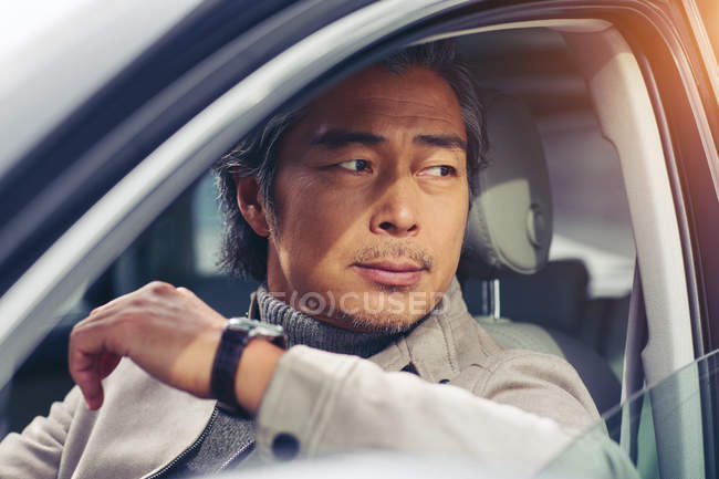 Vue rapprochée de mature asiatique homme assis dans la voiture et regardant loin — Photo de stock