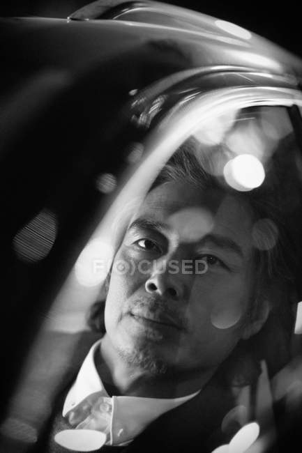 Black and white image of mature asian man driving car and looking at camera, selective focus — Stock Photo