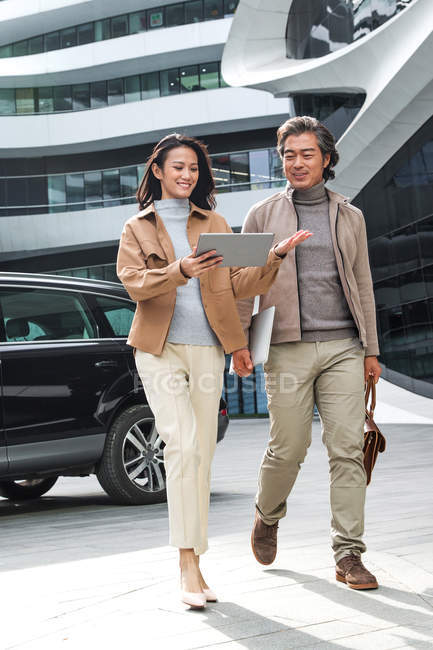Empresários alegres andando e usando tablet perto de centro de negócios moderno — Fotografia de Stock