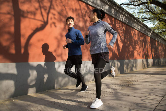 Молода азіатська пара посміхається один одному і бігає разом на вулиці — стокове фото