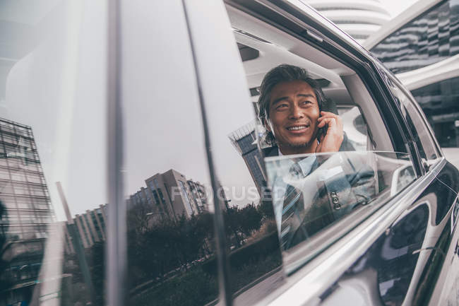Sorrindo maduro asiático empresário sentado no carro e falando por smartphone — Fotografia de Stock