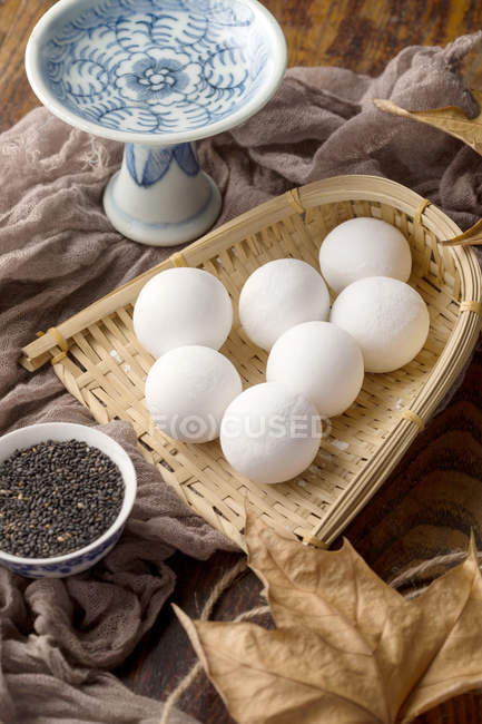Glutinous rice balls in wicker container, dry leaf and sesame seeds on table — Stock Photo