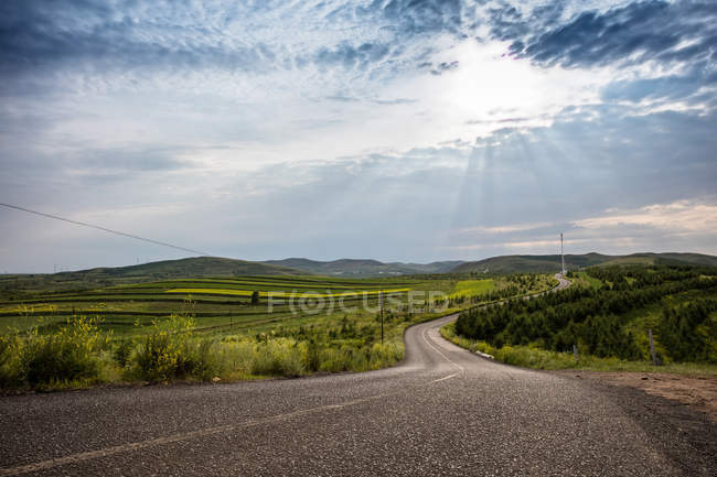 Strada asfaltata vuota, vegetazione lussureggiante e colline panoramiche all'orizzonte — Foto stock