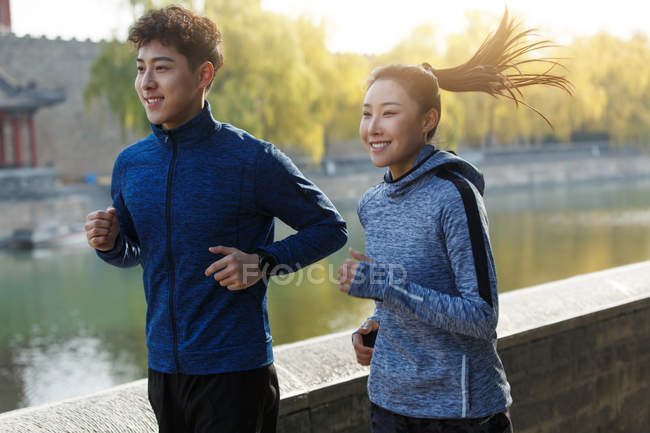 Sorrindo jovem asiático masculino e feminino corredores formação juntos ao ar livre — Fotografia de Stock