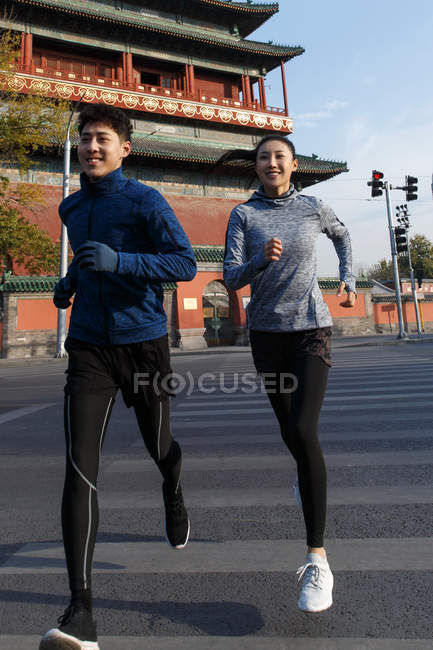 Улыбающийся молодой азиат мужчина и женщина, бегущие вместе по улице — стоковое фото