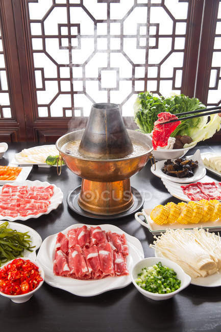 Stäbchen mit Fleisch über Kupfer-Topf und Teller mit verschiedenen Zutaten auf dem Tisch, Scheuern Teller-Konzept — Stockfoto