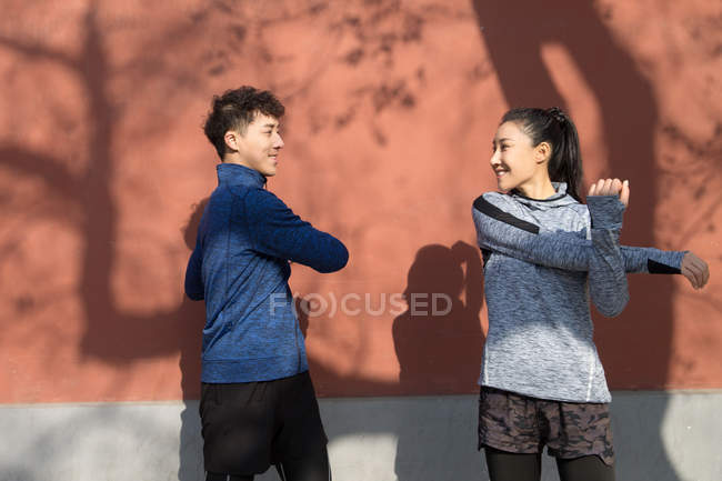 Young male and female athletes in sportswear smiling each other while stretching together on street — Stock Photo