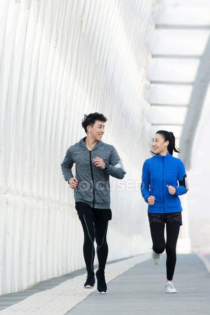 Sportliches junges Paar lächelt einander an und rennt gemeinsam auf Brücke — Stockfoto