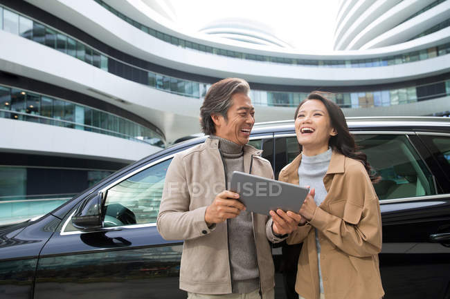 Усміхнені бізнесмени використовують планшет біля автомобіля на парковці сучасного бізнес-центру — стокове фото