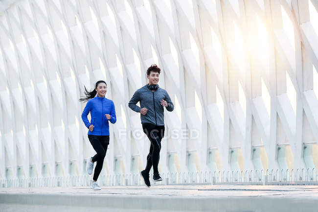 Smiling young asian male and female athletes running together on bridge — Stock Photo