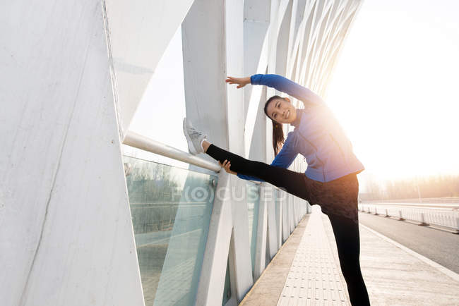 Красивая счастливая молодая женщина в спортивной одежде, растянувшаяся на мосту утром — стоковое фото