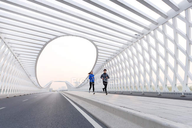 Повнометражний вигляд молодих чоловіків і жінок бігунів у спортивному одязі, що бігають разом на мосту — стокове фото