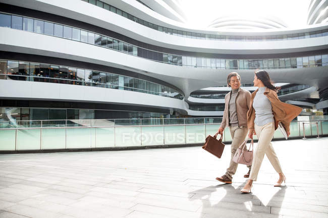 Smiling asian businesspeople walking near modern business center and looking at each other — Stock Photo
