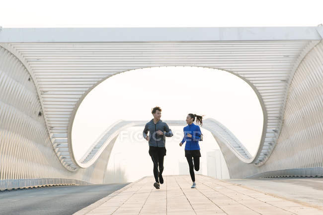Спортивна молода пара посміхається один одному і бігає разом на мосту — стокове фото