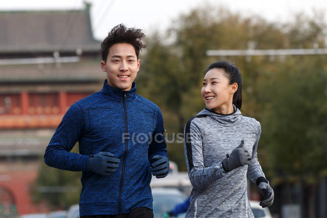 Вид улыбающейся молодой пары, бегущей вместе по улице — стоковое фото