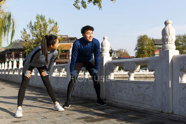 Young asian man and woman in sportswear stretching during workout on street — Stock Photo