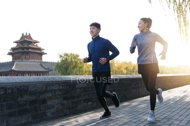 Sorrindo jovens atletas chineses masculinos e femininos em sportswear correndo juntos ao ar livre — Fotografia de Stock