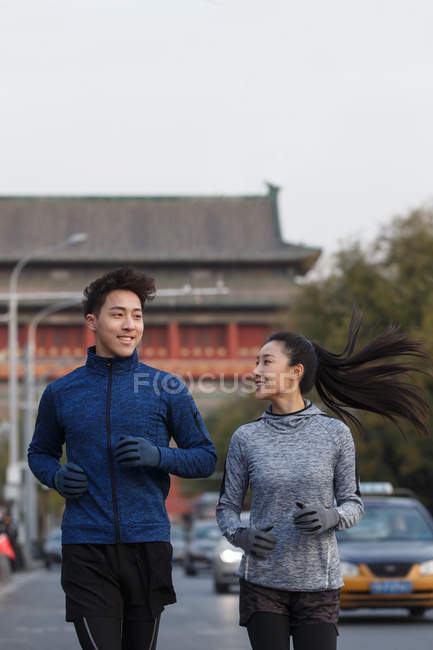 Giovani atleti asiatici in abbigliamento sportivo sorridendo l'un l'altro e correndo insieme per strada — Foto stock
