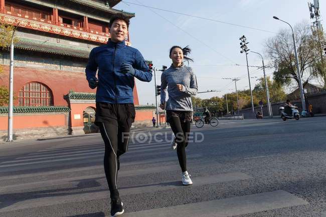Low angle view of smiling young asian runners training together on street — Stock Photo