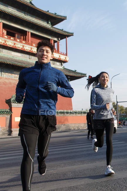 Smiling athletic young couple running together on street — Stock Photo