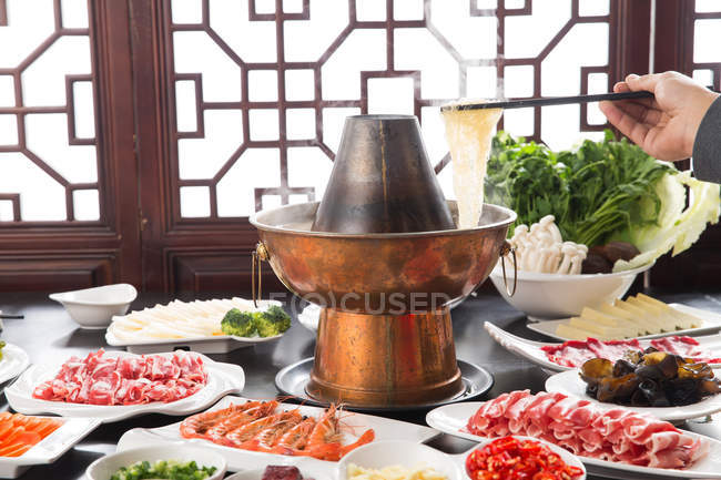 Cropped shot of person holding chopsticks and various ingredients with copper hot pot, chafing dish concept — Stock Photo
