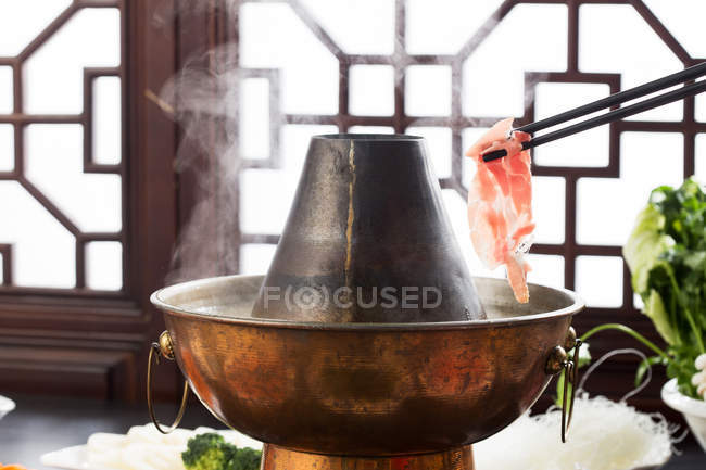 Partial view of person holding chopsticks with meat above copper hot pot, chafing dish concept — Stock Photo