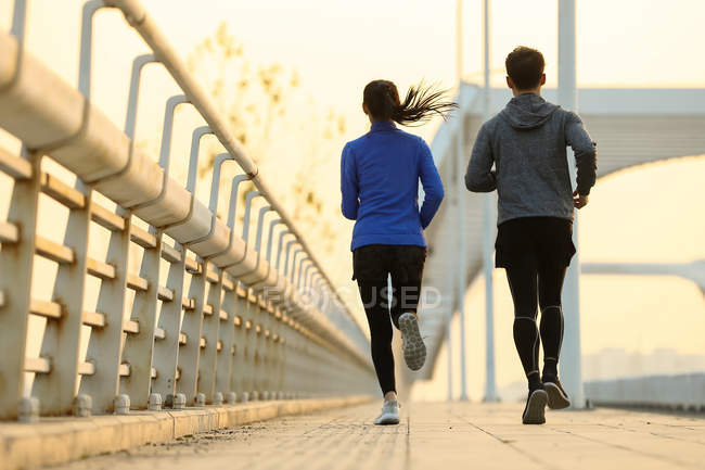 Вид ззаду на молоду пару бігунів, які тренуються разом на мосту вранці — стокове фото