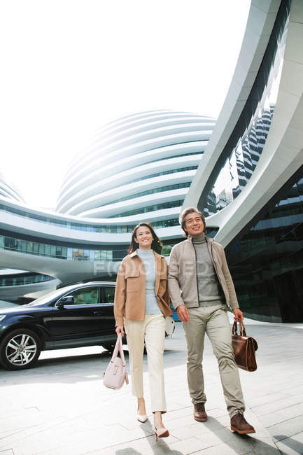 Lächelnde Geschäftsleute, die in der Nähe eines modernen Geschäftszentrums spazieren gehen — Stockfoto