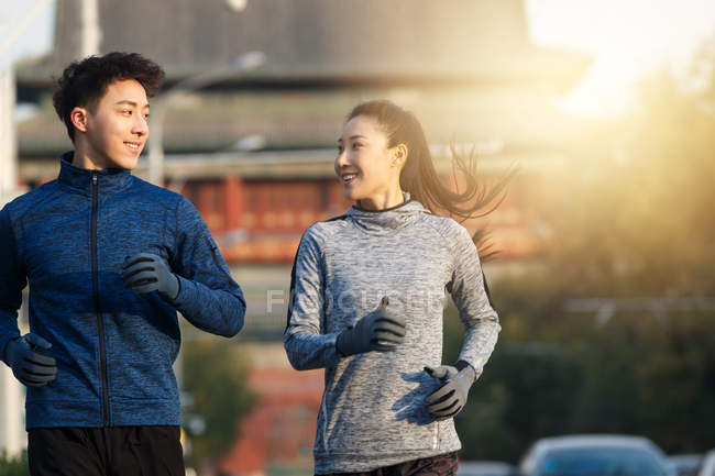Feliz jovem asiático casal de corredores sorrindo uns aos outros na rua — Fotografia de Stock