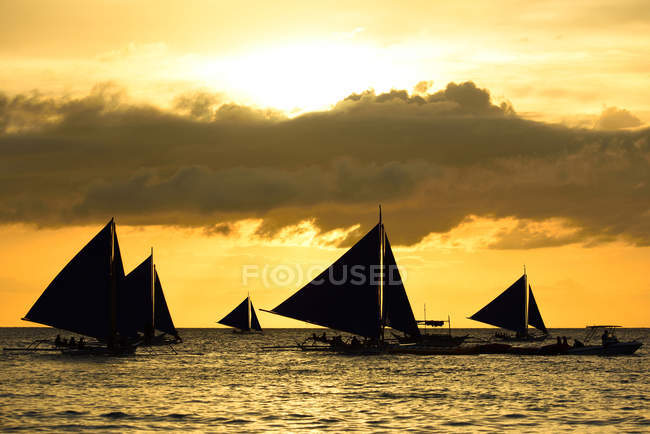 Sagome di barche a vela galleggianti su onde al tramonto scenico — Foto stock