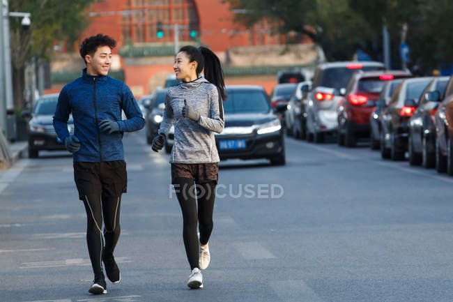 Deportivo joven pareja sonriendo entre sí y corriendo juntos en la calle - foto de stock