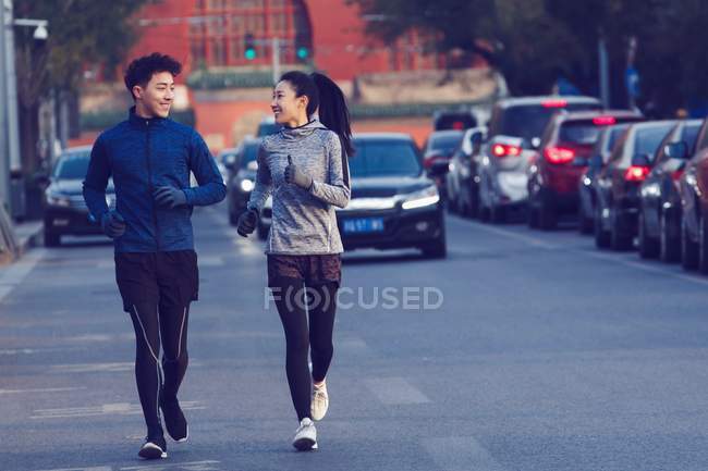 Спортивная молодая пара улыбается друг другу и бегает вместе по улице — стоковое фото