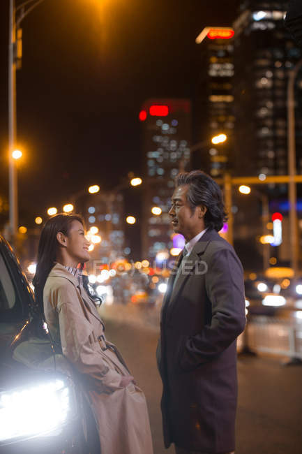Happy asian couple standing near car at evening — Stock Photo