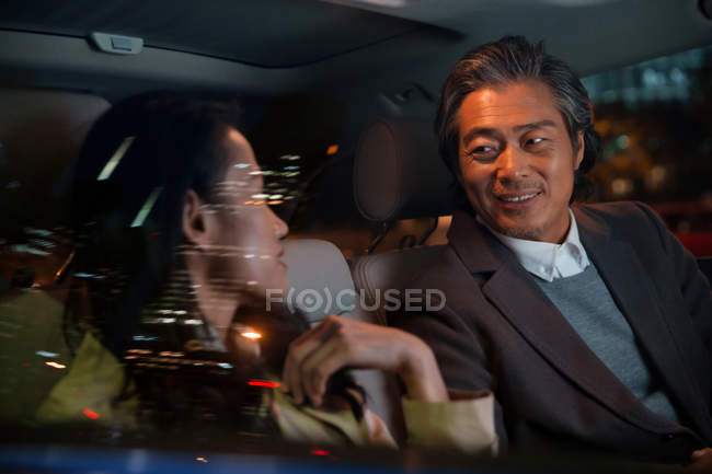 Happy asian couple riding in car and looking at each other at evening — Stock Photo