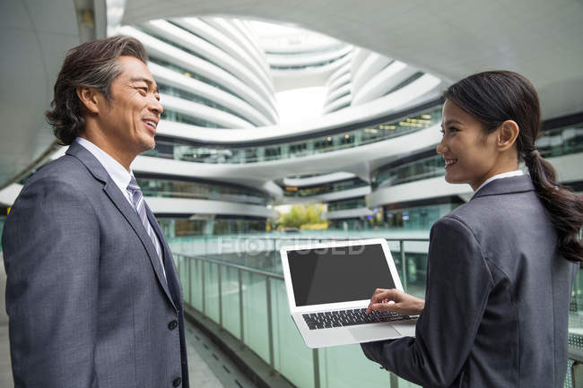 Empresários asiáticos andando com laptop no moderno centro de negócios — Fotografia de Stock