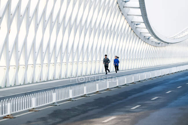 Young couple of joggers in sportswear training together on bridge — Stock Photo