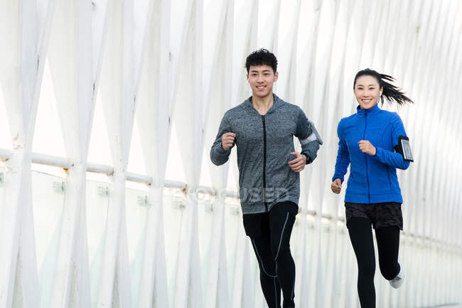 Happy young asian couple in sportswear running together on bridge — Stock Photo