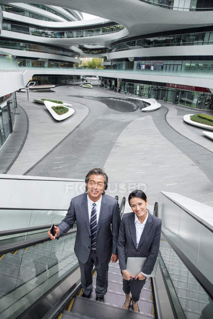 Asiático negocios personas en escalera mecánica en moderno centro de negocios - foto de stock