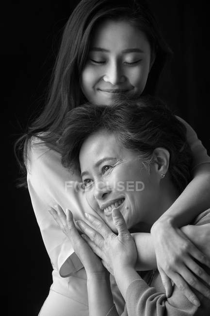 Happy senior mother and young adult daughter hugging on black background — Stock Photo