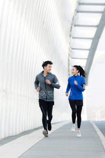 Jeune couple sportif se souriant et courant ensemble sur le pont — Photo de stock