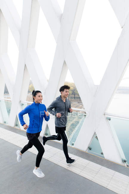High angle view of smiling young asian couple of athletes running together on bridge — Stock Photo