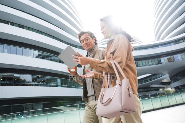 Улыбающиеся бизнесмены гуляющие и пользующиеся планшетом возле современного бизнес-центра — стоковое фото