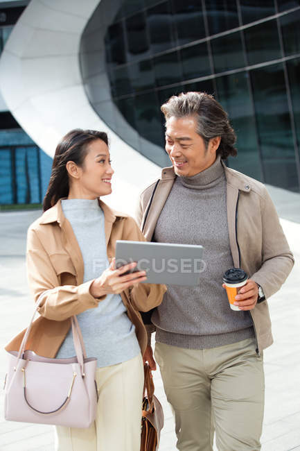 Empresários alegres andando e usando tablet perto de centro de negócios moderno — Fotografia de Stock