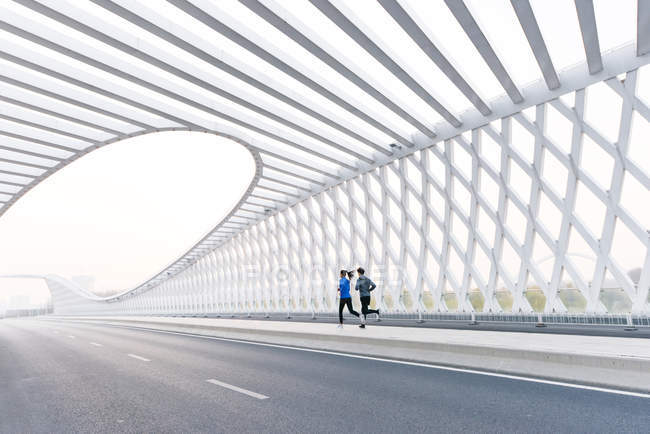 Back view of young athletes in sportswear jogging together on modern bridge — Stock Photo